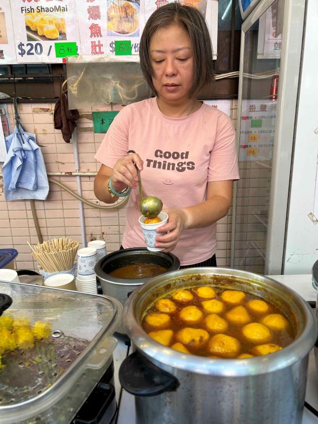 Chinese lady at a food stall ladles fish balls into a cup.