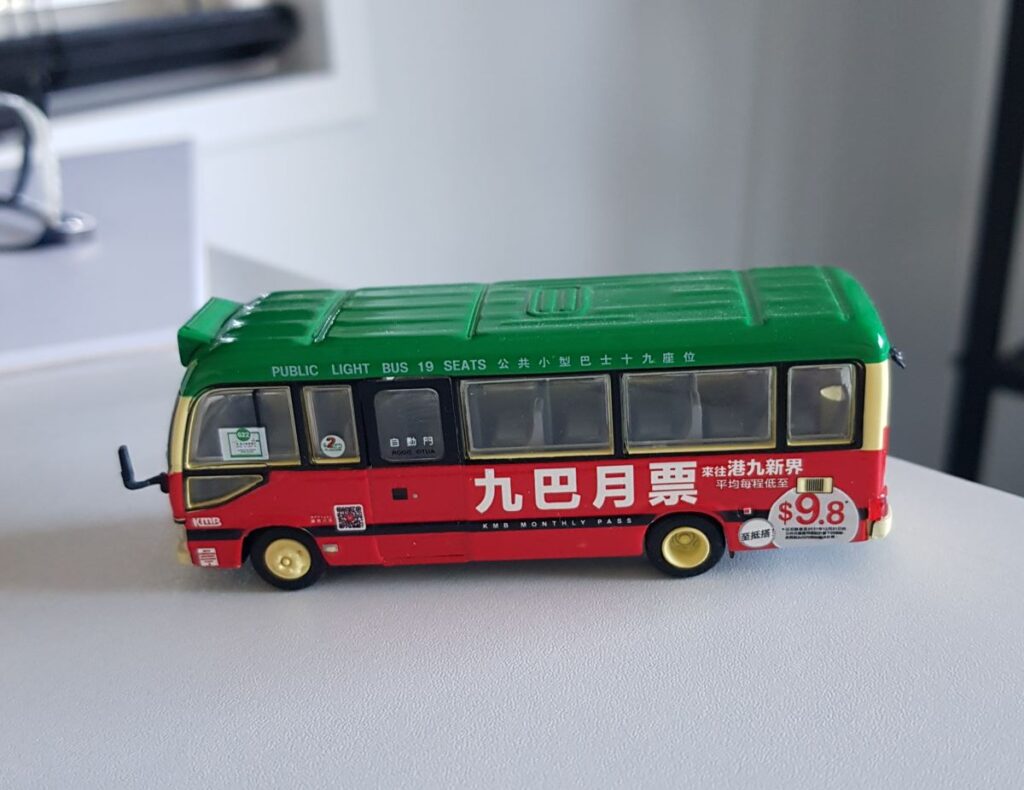 A detailed toy model of a classic Hong Kong green-top public light minibus, with realistic decals showing “KMB Monthly Pass” and a fare sign reading $9.8. This miniature collectible is a popular Hong Kong souvenir that reflects the city’s iconic public transport culture.
