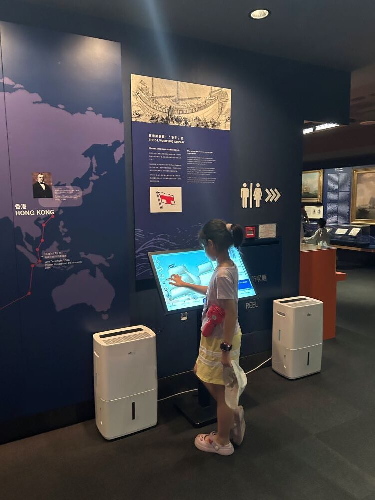 A girl standing in front of an interactive display inside the Hong Kong Maritime Museum.