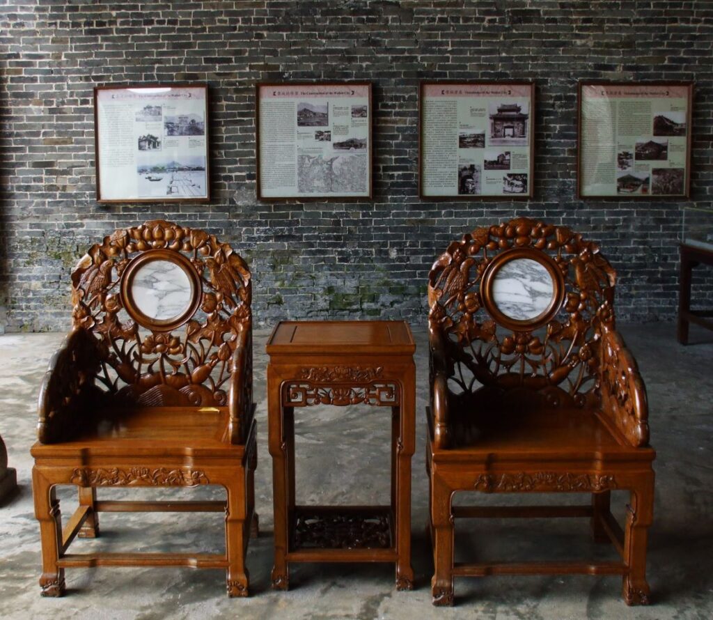 Two Chinese decorative chairs sit side by side. There is four information displays on the wall behind the chairs.