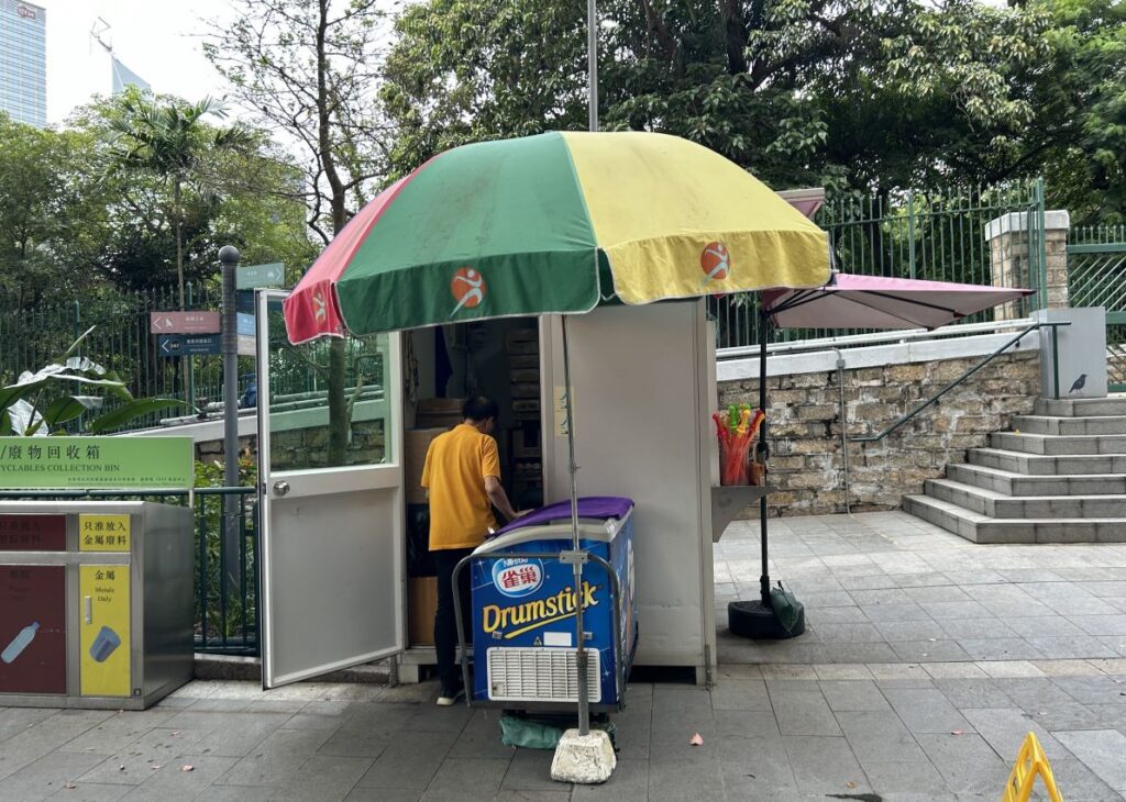 A man stands under an umbrella at an Ice cream shop.