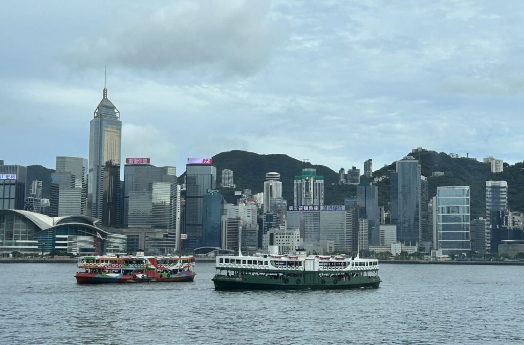Two passenger boats called the Hong Kong Star Ferry cross in Victoria Harbour. The Hong Kong skyline is in the background.